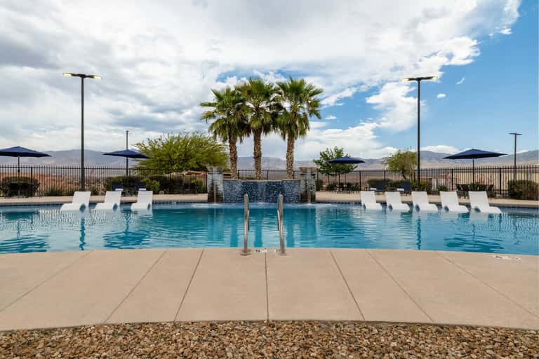Resort pool with waterfall feature, loungers, palm trees, and mountain landscape