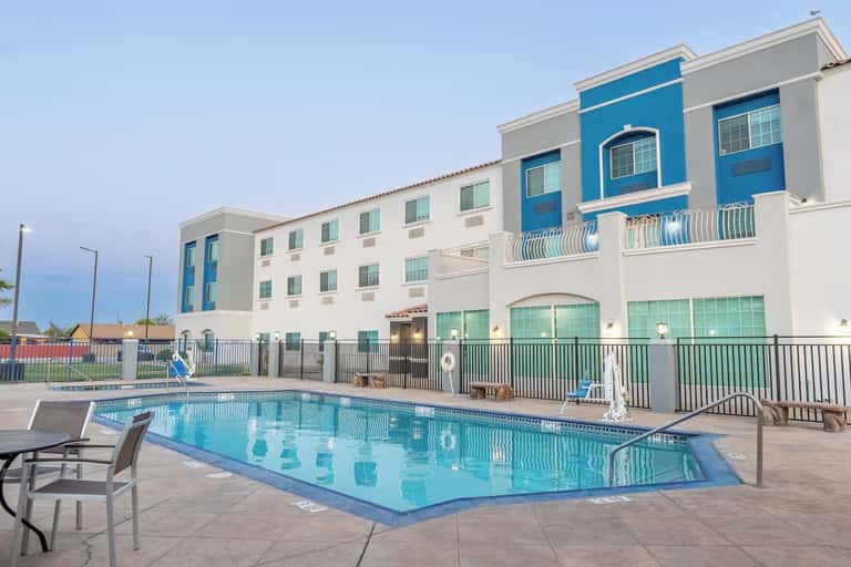 Contemporary hotel exterior with blue and white facade, swimming pool, lounge chairs, and metal fencing