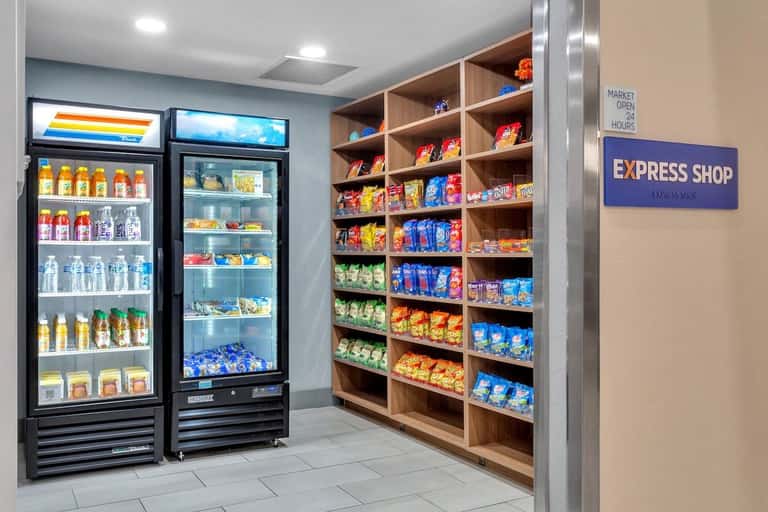 Hotel express shop with refrigerated beverage cases and wooden shelving stocked with snacks and drinks