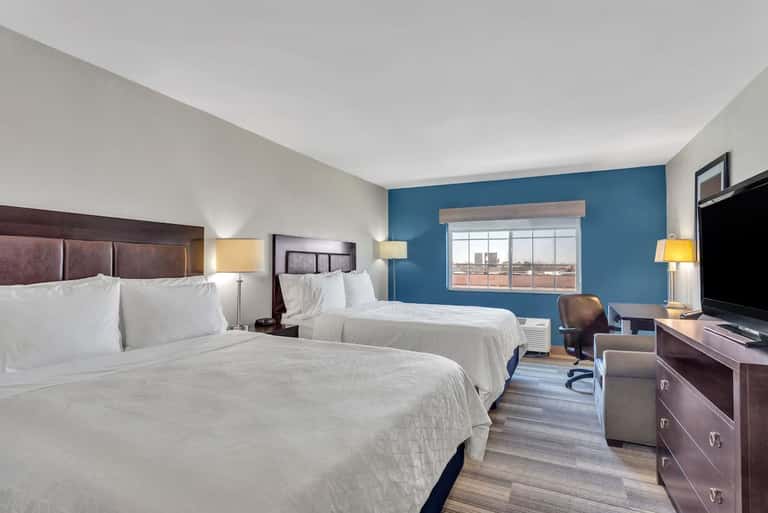 Hotel double queen bedroom with blue accent wall, work area, flat-screen TV, and large window with city view