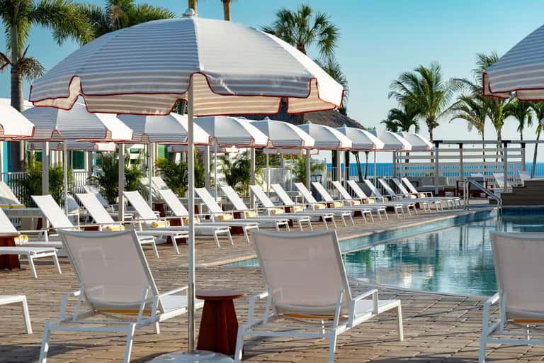 Pool deck with striped umbrellas, lounge chairs, and palm trees at waterfront resort