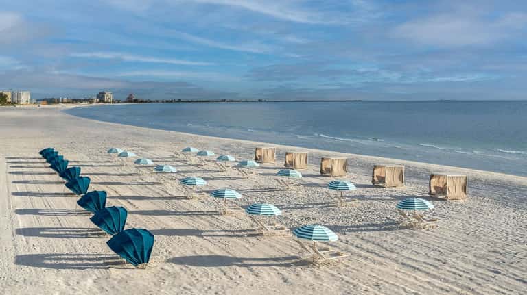 Beach setup with blue and teal umbrellas, loungers, and tan cabanas along sandy shore with calm ocean