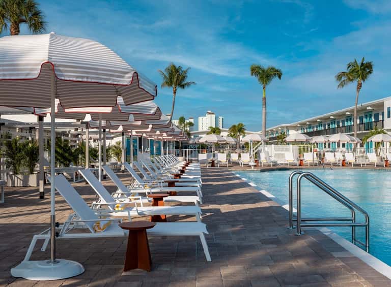 Pool area with red and white striped umbrellas over loungers, covered pergola seating, and hotel towers