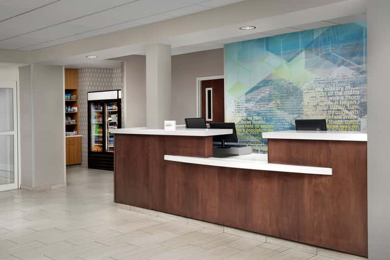 Modern hotel lobby with dark wood reception desk, beverage coolers, and informational wall mural