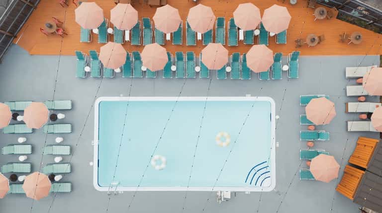 Overhead view of rectangular pool surrounded by teal loungers and peach umbrellas on deck