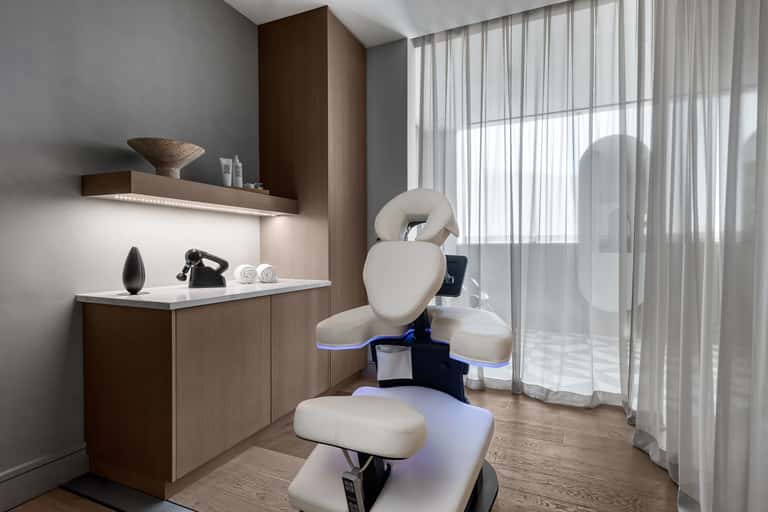 Professional spa treatment room with white massage chair, wooden cabinetry, and sheer curtains