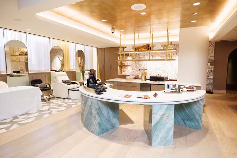 Upscale spa reception area with marble desk, suspended lighting, and wavy wall patterning