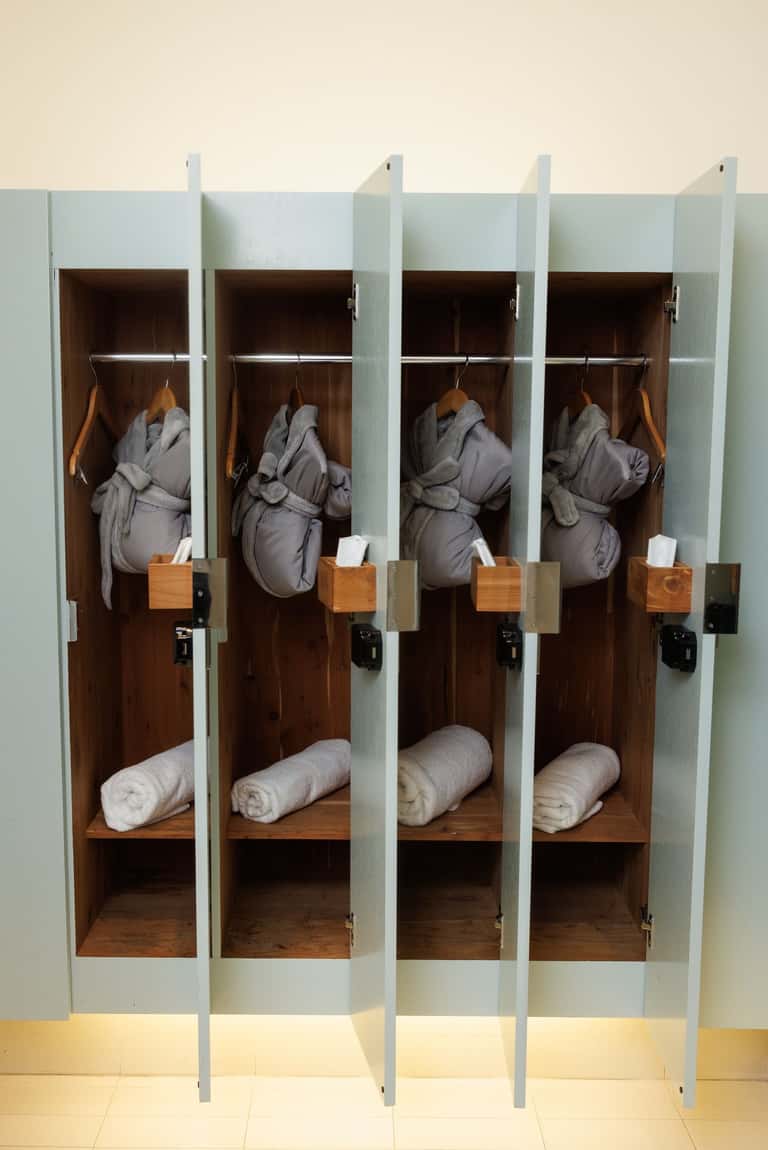 Individual locker storage with glass doors displaying gray robes and rolled white towels