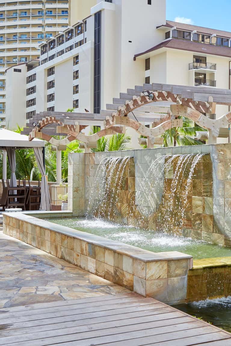 Wooden pergola with water feature waterfall and modern hotel buildings in background