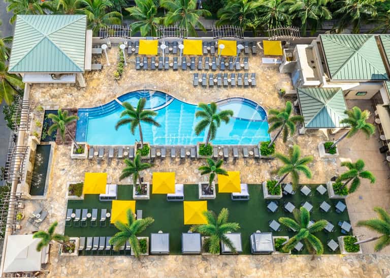 Aerial view of resort pool with yellow umbrellas, loungers, and surrounding palm trees