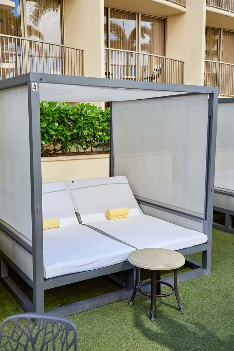Modern gray daybed with white mattress and yellow pillows in private cabana with retractable screens