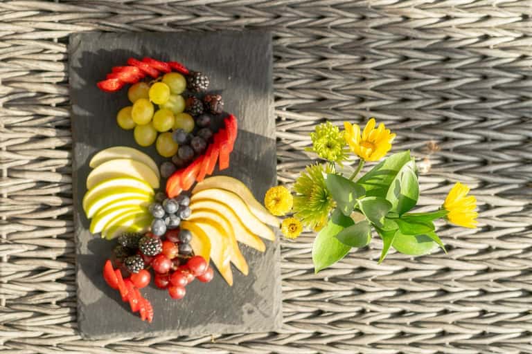 Fruit and berry arrangement on dark slate with yellow flowers on woven placemat