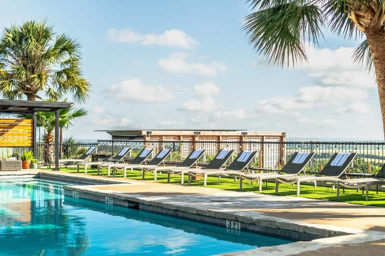 Resort pool with lounge chairs on lawn and pergola structure with wooden screening