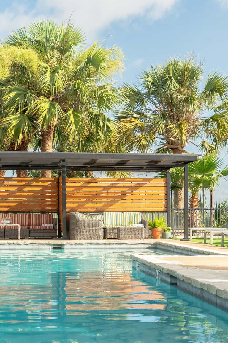 Pool area with modern pergola, palm trees, and wicker lounge seating at resort