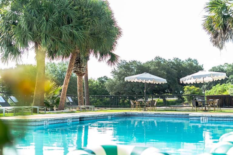 Resort pool with white umbrellas, palm trees, and metal railing overlooking landscape