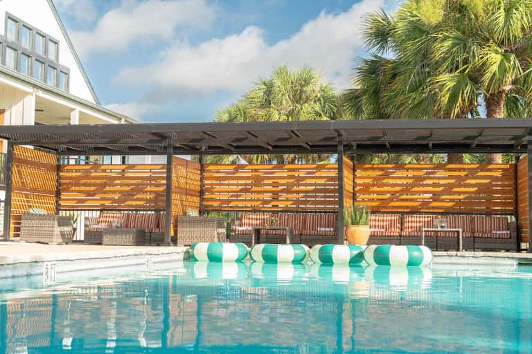 Resort swimming pool with green and white striped floats lined along modern covered lounge structure