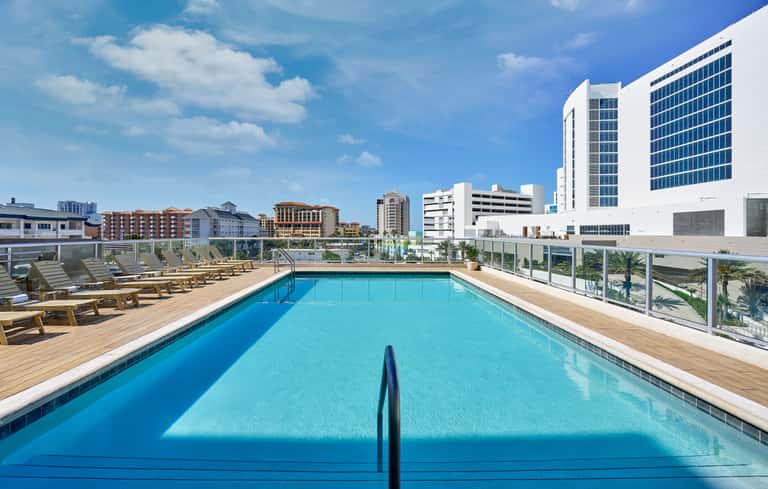 Rooftop infinity pool with lounge chairs overlooking downtown cityscape and blue sky