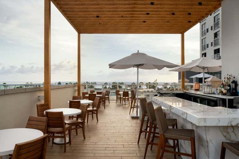 Covered rooftop bar and dining area with umbrellas, tables, and ocean horizon views