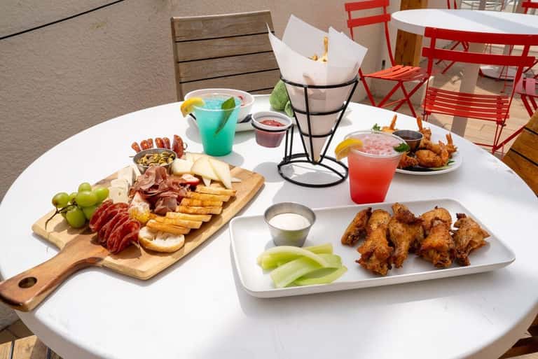Outdoor dining table with charcuterie board, fried appetizers, and colorful cocktails
