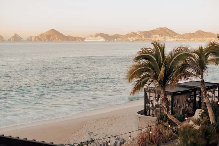 Beach cabana with palm trees overlooking bay with rocky islands and cruise ship at sunset