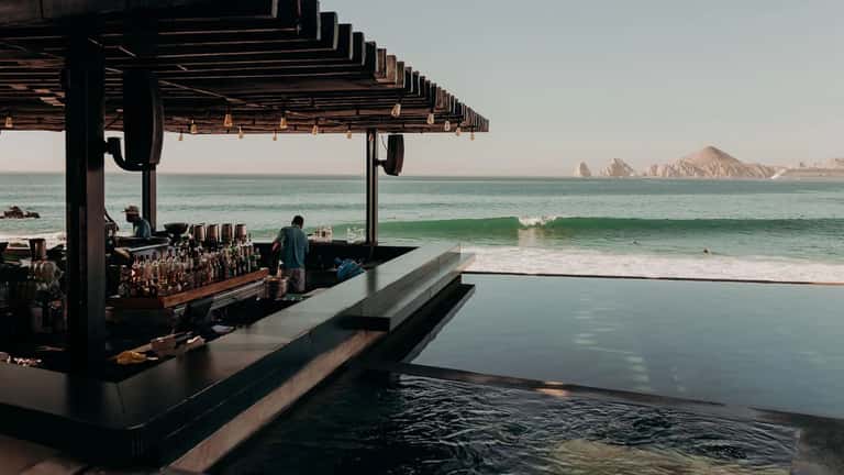 Beachfront bar with swimming pool, waves, and rocky island formations in background