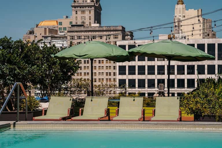 Resort pool with lounge chairs, green umbrellas, and historic buildings
