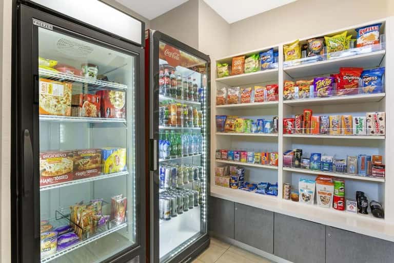 Hotel convenience store with refrigerated freezers stocked with frozen foods and beverages, and shelves displaying snacks and drinks