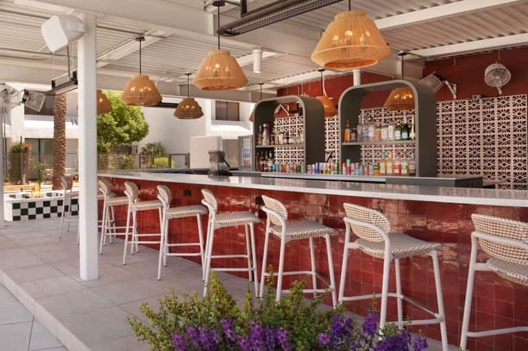 Outdoor bar with woven pendant lights, red counter, and geometric screens