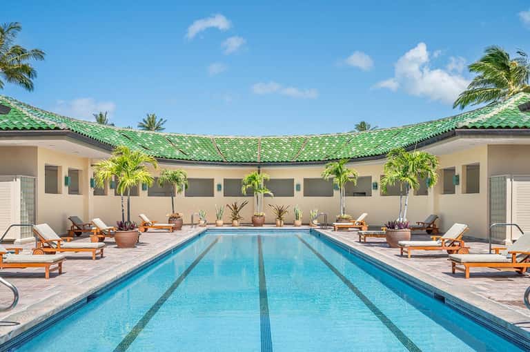 Rectangular lap pool with lane markers surrounded by wooden lounge chairs and potted plants in a courtyard with green tile roof
