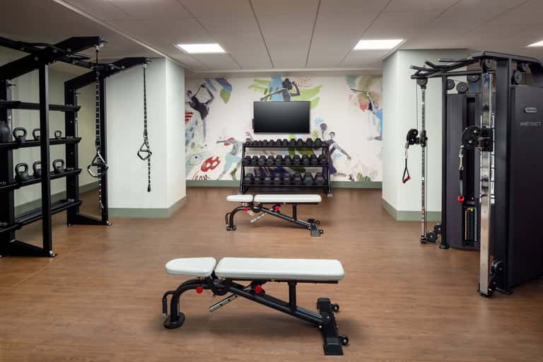 Modern fitness facility with weight rack, exercise benches, cable machines, and motivational wall mural