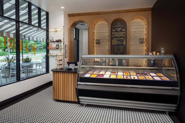 Modern gelato shop interior with wooden arched display cases, counter, and large windows overlooking outdoor seating