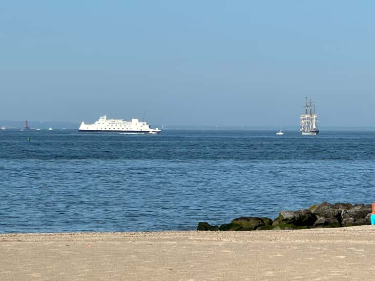 Ocean beach view with cruise ship and tall ship sailboat on horizon