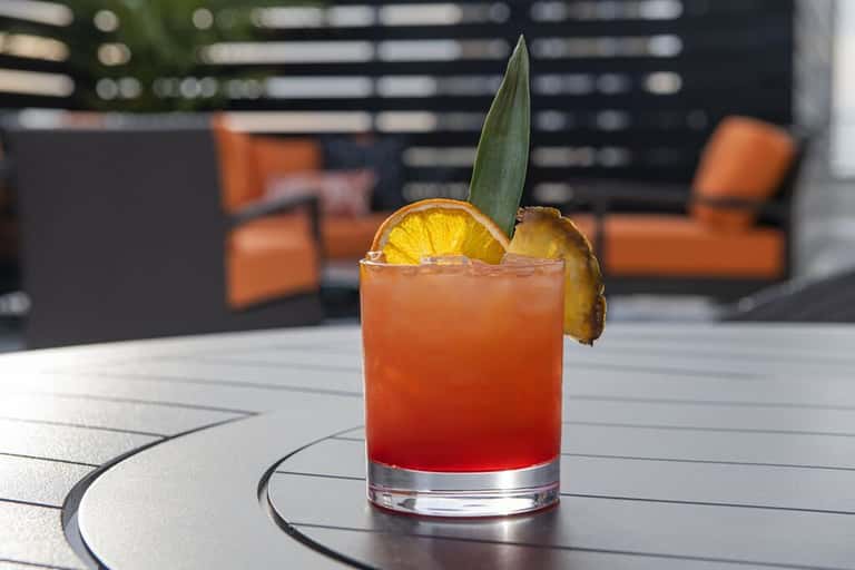 Tropical cocktail with pineapple garnish and green leaf on outdoor patio table