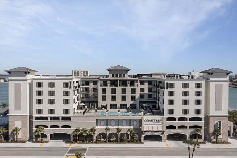 Waterfront resort building with white facade, palm trees, and covered entrance