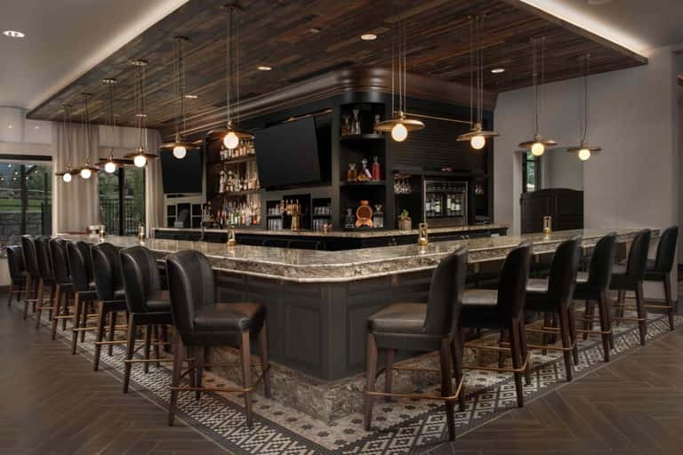 Upscale bar lounge with granite countertop, pendant lighting, dark wood ceiling, and black leather seating