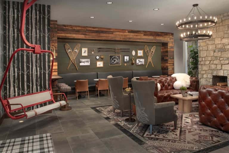 Mountain lodge lobby with red ski lift sculpture, leather seating, rustic wood beams, and modern chandelier