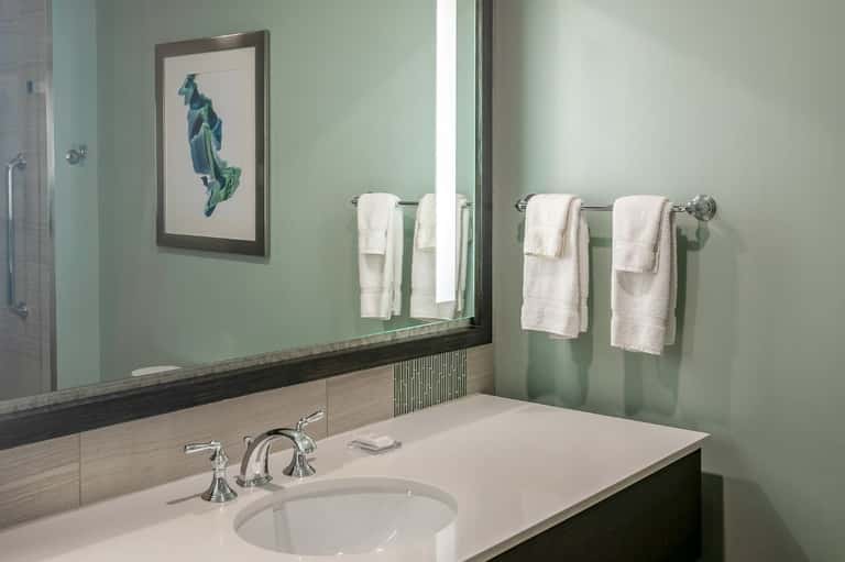 Spa bathroom with soft green walls, white sink, framed sailboat artwork, and chrome fixtures