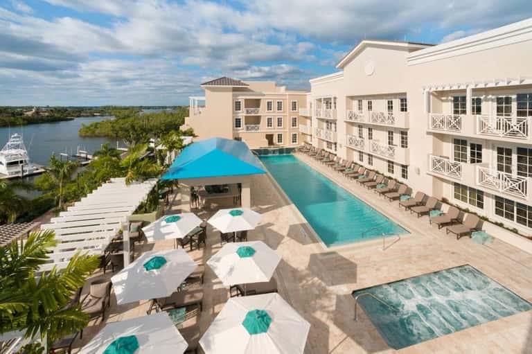 Aerial view of waterfront resort with infinity pool, lounge chairs, beach umbrellas, and river views