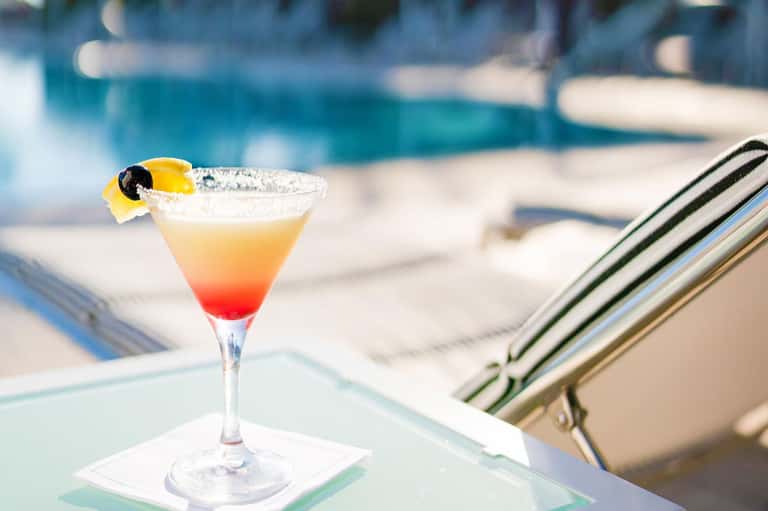 Gradient cocktail with lemon slice and black olive by pool lounge chair