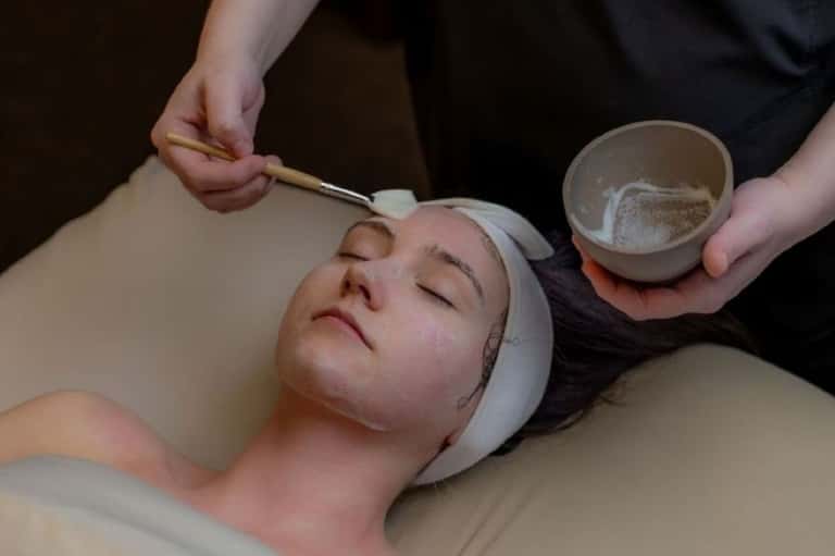 Spa therapist applying facial treatment mask to client's face with brush applicator
