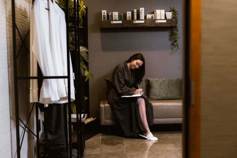 Spa receptionist writing notes at consultation desk in modern spa interior with shelving