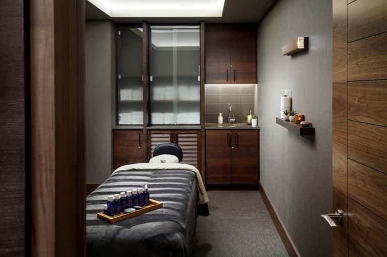 Professional massage treatment room with wooden cabinetry, treatment bed, and amenity bottles