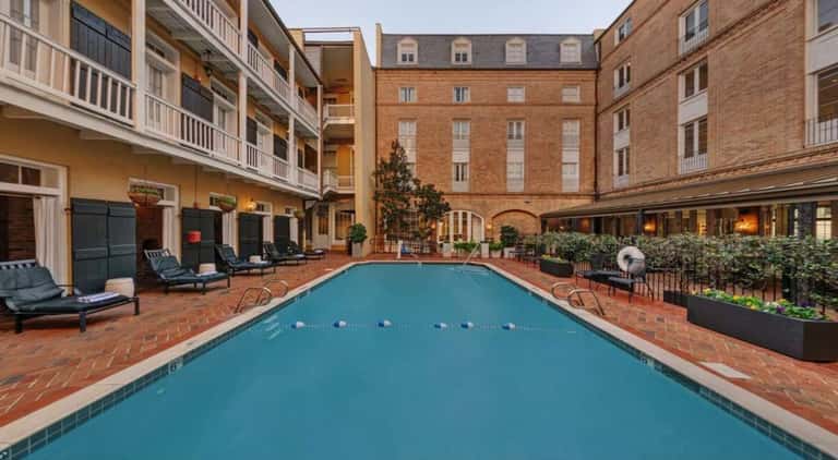 Indoor lap pool in brick courtyard with lounge chairs, plants, and surrounding residential architecture