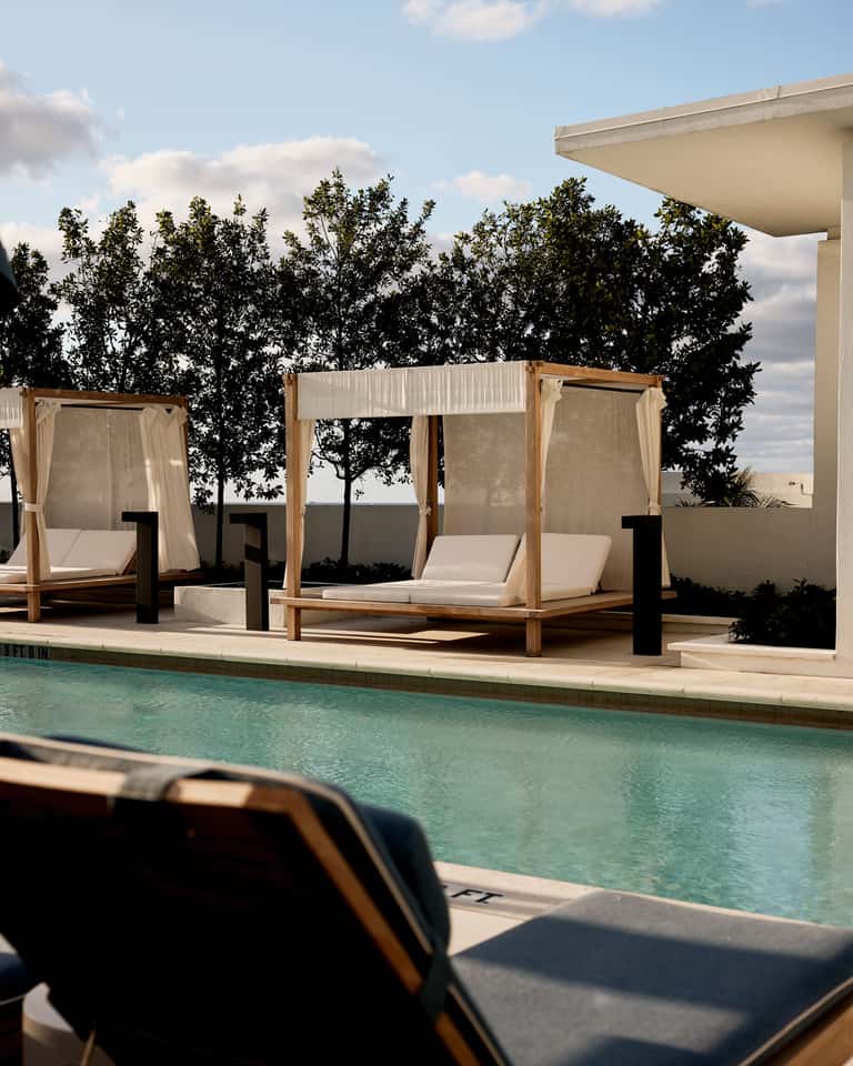 Luxury poolside cabanas with white curtains overlooking landscaped grounds and clear blue pool