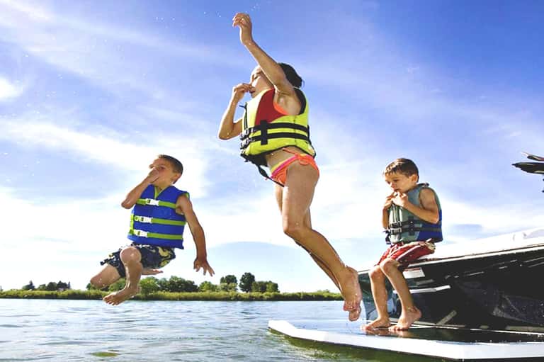 Man and two boys in life jackets jumping from boat into river on sunny day