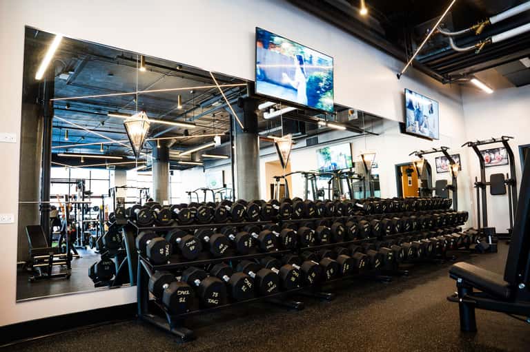 Modern fitness center with extensive dumbbell collection, cardio equipment, and TV screens