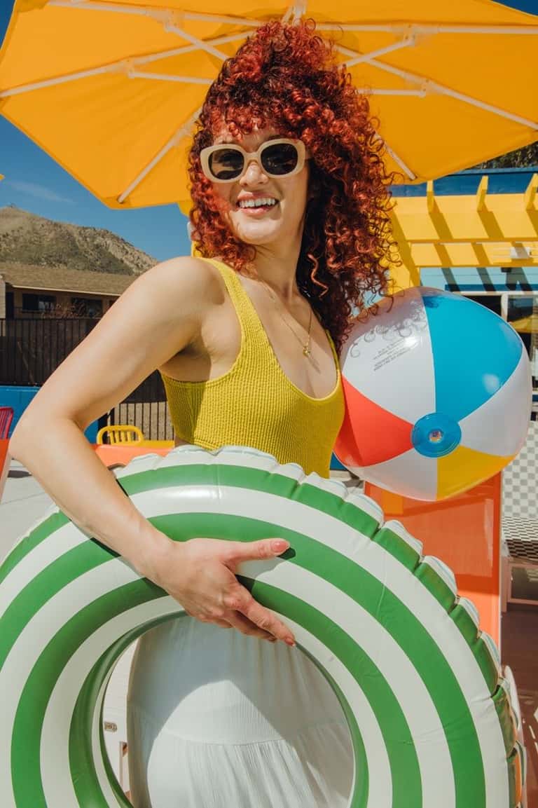 Woman enjoying pool area under yellow umbrella wearing yellow swimwear and white sunglasses
