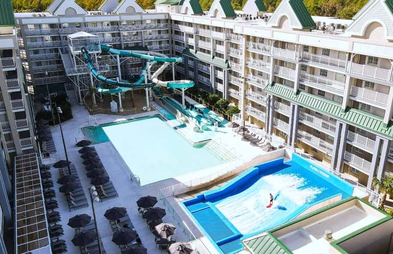 Aerial view of water park with turquoise slides, white swimming pool, black lounge chairs, and multi-story resort buildings
