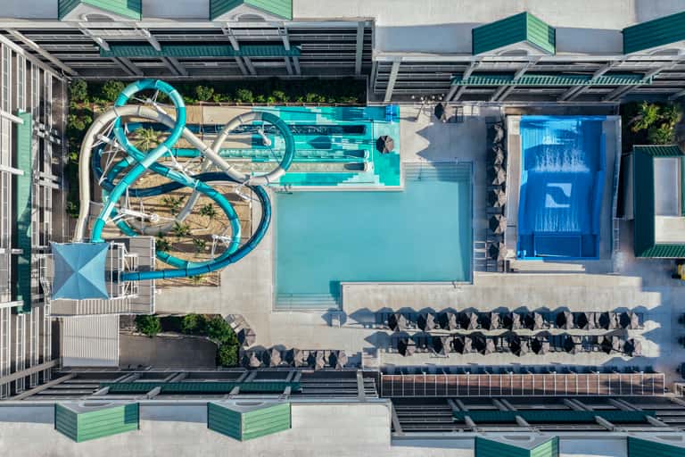 Overhead view of resort pool area with turquoise water slides, lounge chairs, and solar panel canopy