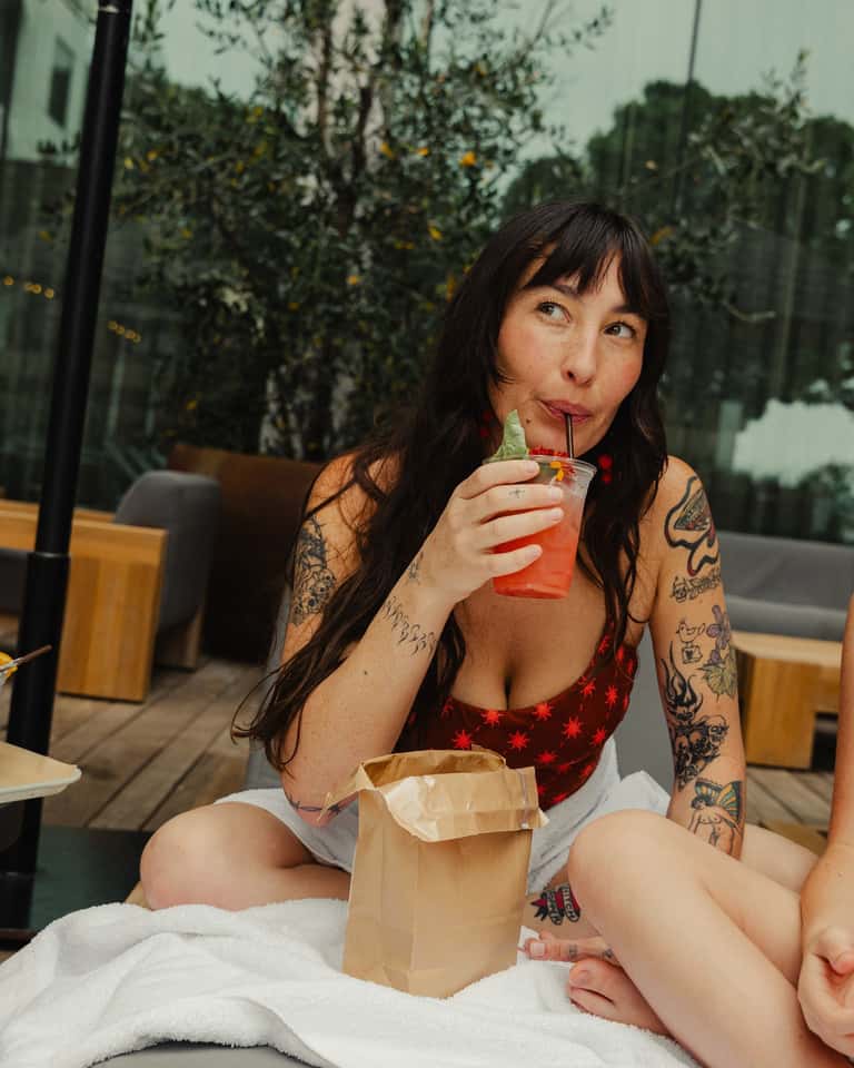 Woman in red bikini enjoying a colorful beverage poolside on a sunny day with natural backdrop